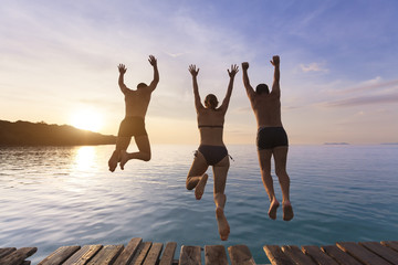 Group of people having fun jumping in water from pier