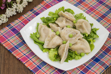 Dumplings with minced chicken on a plate  fresh herbs and peas. Wooden background. Close-up
