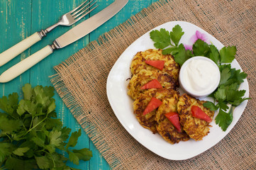 Zucchini Pancakes with sour cream, tomatoes and herbs. Wooden background. Close-up. Top view