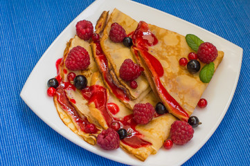 Pancakes with raspberries, currants, sugar and mint. On the blue table. Top view. Close-up