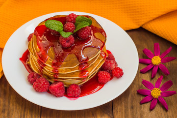 Pancakes with raspberry jam and fresh berries. Wooden background. Close-up