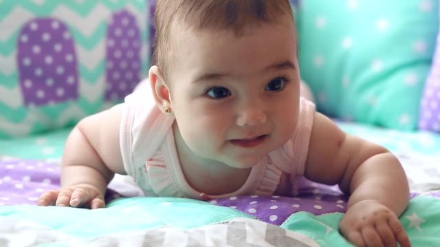 Beautiful happy little girl lying in a crib on his stomach and laughs