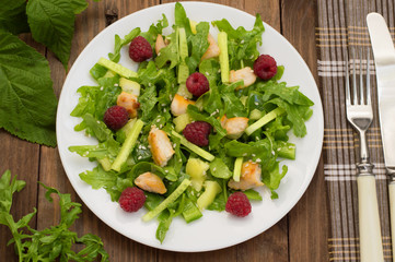 Salad with raspberries, arugula, cucumber, paprika, roasted chicken and sesame. Wooden background. Close-up
