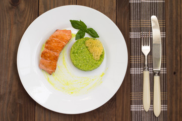 Grilled salmon steak with pea puree, cheese crisps and basil on a plate  the sauce. Wooden rustic background. Top view. Close-up