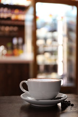 Cup with hot tasty coffee on wooden table in cafe, close up view