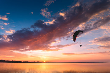 Silhouette de parapente volant au-dessus du coucher de soleil sur la mer
