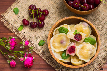 Dumplings with a cherry and mint leaves on  background of flowers  burlap. Wooden table. Top view. Close-up