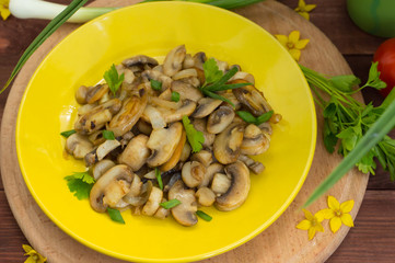 Fried mushrooms on a yellow plate. Wooden background. Top view. Close-up