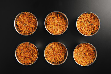 Set of six small steel pans with crumble desert on reflective black surface shot from the top
