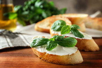 Delicious bruschetta with cream cheese and basil on wooden table, closeup