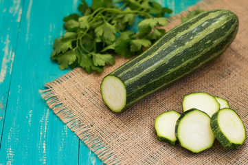Zucchini, fresh and chopped slices on sackcloth with greens. Wooden turquoise background. Top view. Close-up