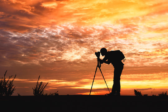Silhouette image of a photographer with a sunset background .