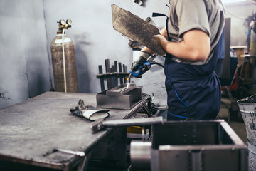 Factory for production of heavy pellet stoves and boilers. Close up shot of manual worker's hand welding some parts.