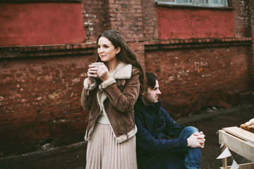 Young happy couple laughing and enjoying christmas street decorations with gifts in craft paper, cookies, cacao, handmade wooden table and red brick wall