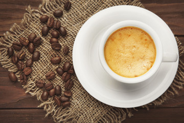 Cup of tasty coffee and beans on wooden table