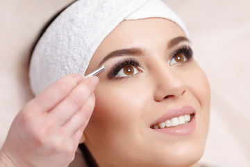 Young woman tweezing her eyebrows in beauty saloon