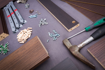 Furniture components and tools like a hammer and screwdriver flat lay on gray background of material.