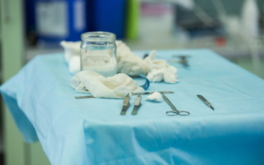Surgical instruments and gauze swabs on a tray during surgery in hospital operating room. Cosmetic surgeon operating a patient. Forceps and tweezers during surgery.