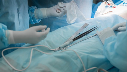 Close-up image of surgeon performing cosmetic plastic surgery on breasts in hospital operating room. Breast implant, augmentation, enlargement, enhancement. Doctor holding surgical forceps, tweezers.