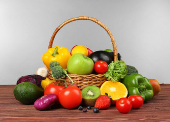 Set of different fruits and vegetables in wicker basket on light background