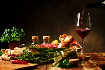 Fresh raw meat with herbs, glass of red wine and vegetables