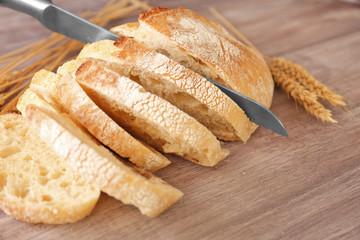 Sliced bread with knife and wheat spikes on wooden table closeup
