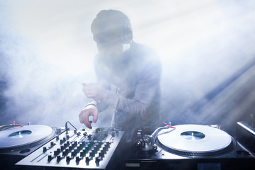 Club DJ playing mixing music on vinyl turntable at party from nightlife lights
