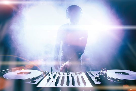 Club DJ playing mixing music on vinyl turntable at party from nightlife lights