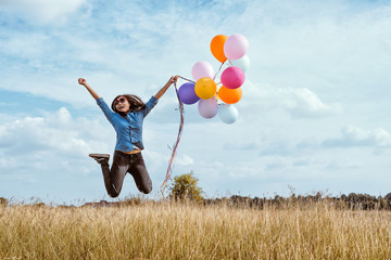 Woman in blue shirt jumping with colorful balloons in the meadow