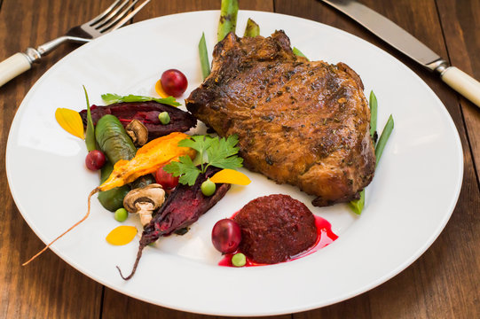 Fried Grilled pork steak on the bone with vegetables, mashed beetroot and berry sauce. Wooden background. Top view. Close-up