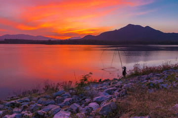 View of Mae Moei reservoir with a fisherman dipping his dip fishing net during twilight time of the day.