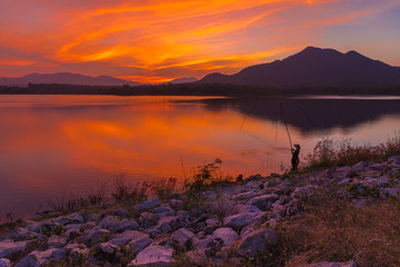 View of Mae Moei reservoir with a fisherman dipping his dip fishing net during twilight time of the day.