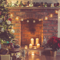 Christmas setting background: decorated Christmas tree, pine cones in the basket, wooden trees, poinsettia with fireplace on the background; candles and lights, selective focus. Toned photo