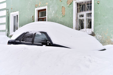 Car covered with snow in the courtyard of apartment house