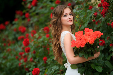 Obraz na płótnie Canvas Beautiful young woman with red flowers posing in the rose garden