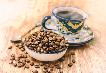 Organic coffee grains and a colorful hand painted coffee cup over wood table