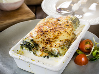 Lasagna in ceramic casserole dish served with tomato and herb, Italian food