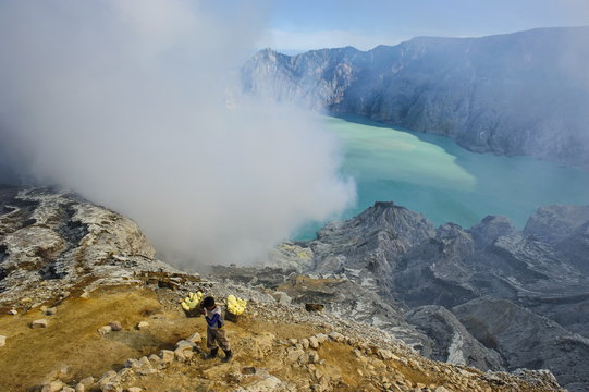 Worker loaded with big pieces of sulphur in front of steam clouds on the Ijen crater lake, Java, Indonesia