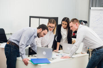 Young business people sitting in office during meeting and discussing with paperwork using laptops