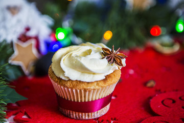 Пирожное, стоит на красная новогодней салфетке на белом деревянном столе в окружении зеленой новогодней гирлянды и огней, игрушки Санта клаус, имбирных пряников в виде звезды, гранат, сушеного лимон - obrazy, fototapety, plakaty