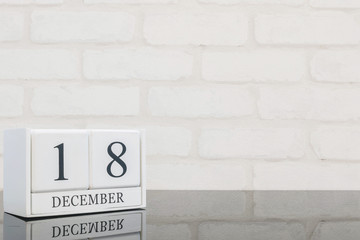 Closeup white wooden calendar with black 18 december word on black glass table and white brick wall textured background with copy space , selective focus at the calendar