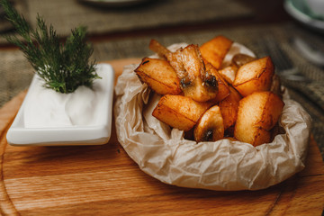 Fried Potatoes with Mushrooms rural and sour cream sauce on a wooden stand in restaurant