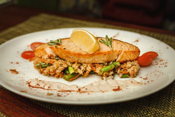 Salmon steak grilled with rice and various vegetables and a lemon on a plate in a restaurant, ready to eat.
