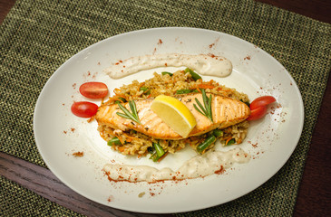 Salmon steak grilled with rice and various vegetables and a lemon on a plate in a restaurant, ready to eat.