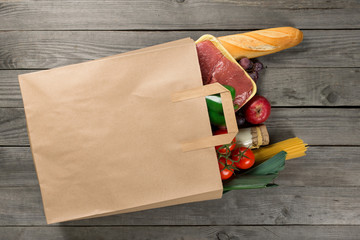 Paper bag full of different food on wooden background