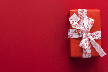 big holiday present wrapped in bright red kraft paper with white tape on red vinous background