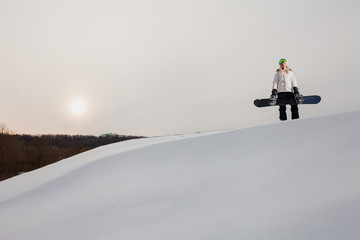 Young woman and her snowboard on snow-covered mountainside at sunset