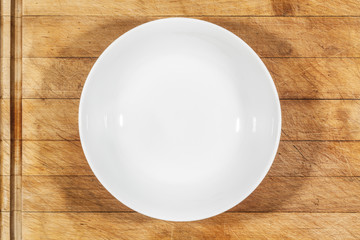 Deep white small soup plate on wooden cutting board from above