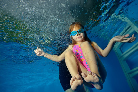 Sports little girl swims and trains underwater in the pool on a blue background. Portrait. Close-up. The view from under the water at the bottom. Landscape orientation