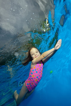 Sports little girl swims underwater in the pool with their hands stretched out and smiling. Shooting under water. Vertical orientation